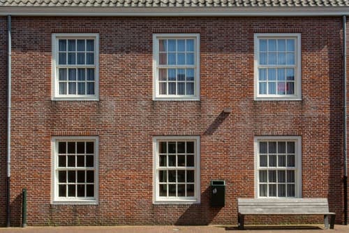 Front view of a brick building facade with sash windows and a wooden bench.